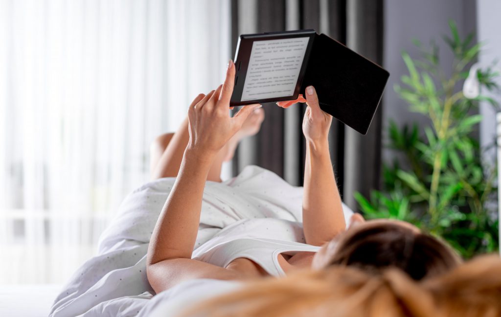 woman reading the post office girls by Poppy Cooper in bed, on her kindle