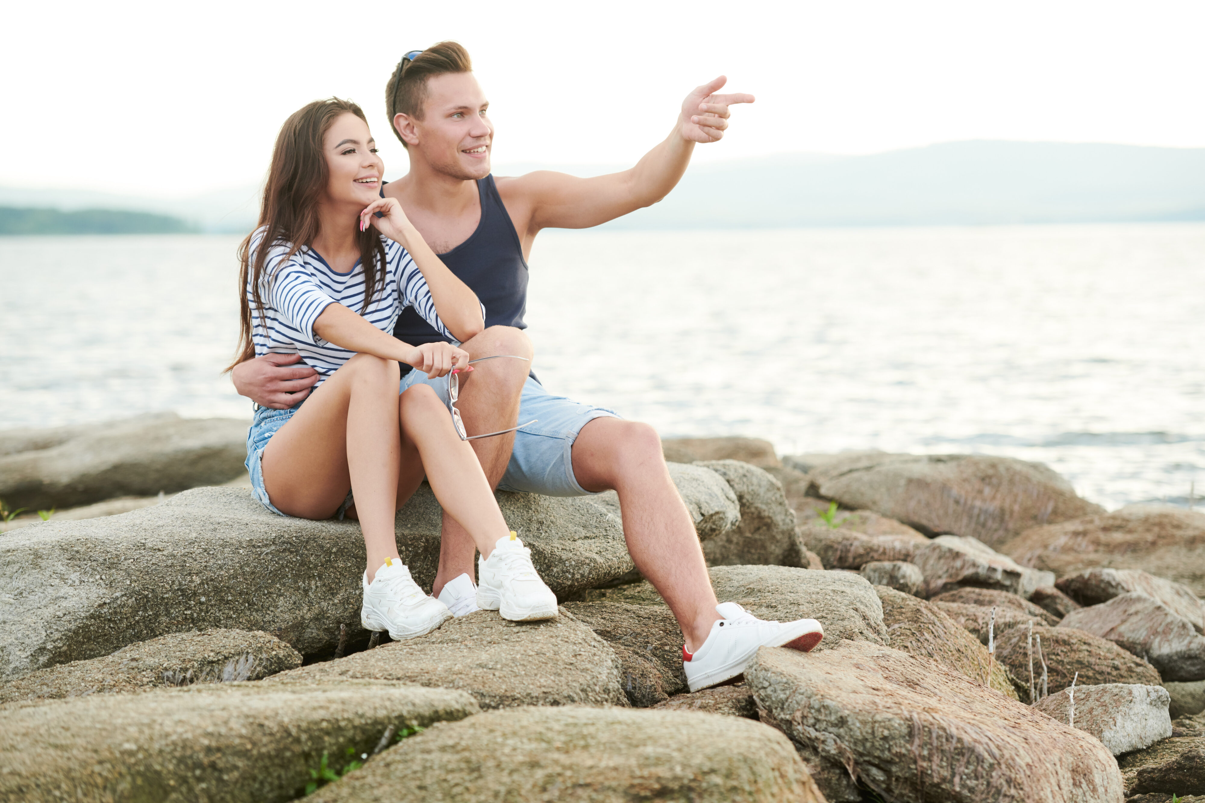 Young couple sat on rocks at the beach, wondering do holiday romances ever last?